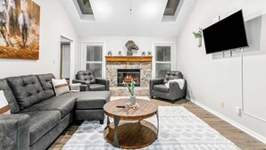 A living room with a sectional sofa, two armchairs, a fireplace, a flat-screen TV, and a ceiling fan. - Home Near Legends_Sleeps 8_Great Location_Shops (Kansas City)