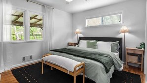 A bedroom with a bed, a bench, a ceiling fan, a window, and a nightstand. - Kid-Friendly Home w/ Yard & Workspace (Shawnee)