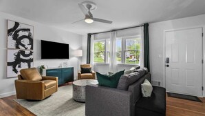 A modern living room with a sofa, armchair, and a TV mounted on the wall. - Kid-Friendly Home w/ Yard & Workspace (Shawnee)