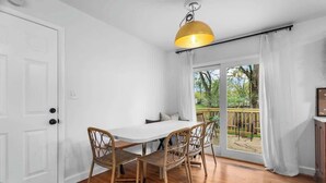A dining area with a white table and wicker chairs, a yellow pendant light, and a view of a deck and greenery outside. - Kid-Friendly Home w/ Yard & Workspace (Shawnee)