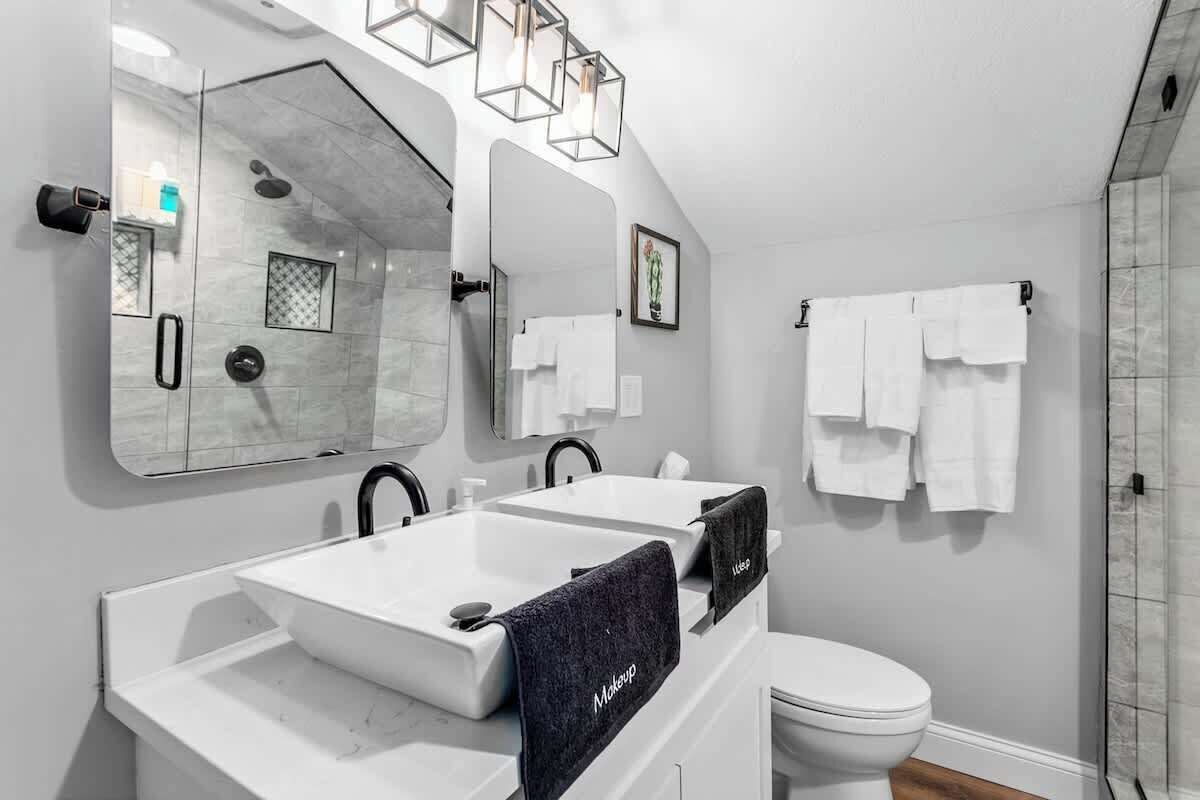 Un baño moderno con un espejo grande, dos lavamanos, un inodoro y una ducha.