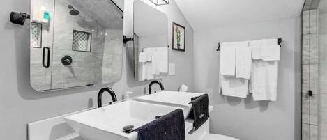 Un baño moderno con un espejo grande, dos lavamanos, un inodoro y una ducha.