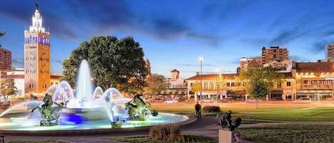 Una plaza urbana con una fuente, una torre del reloj y edificios históricos.
