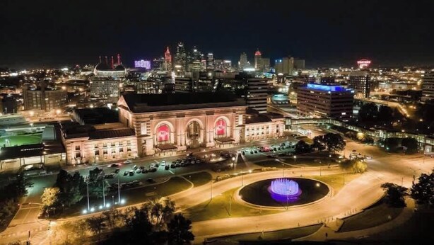 A large, historic building with a central courtyard and a fountain, surrounded by modern cityscape and illuminated buildings. - Great Stay_3BR Home_Walk to downtown Lee's Summit (Lee's Summit)