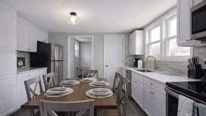 A modern kitchen with white cabinets, a dining table set for four, and a black stove. - Great Stay_3BR Home_Walk to downtown Lee's Summit (Lee's Summit)