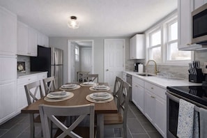 A modern kitchen with white cabinets, a dining table set for four, and a black stove. - Spacious 3BR Home_Walkable_FIFA WC26 (Lee's Summit)