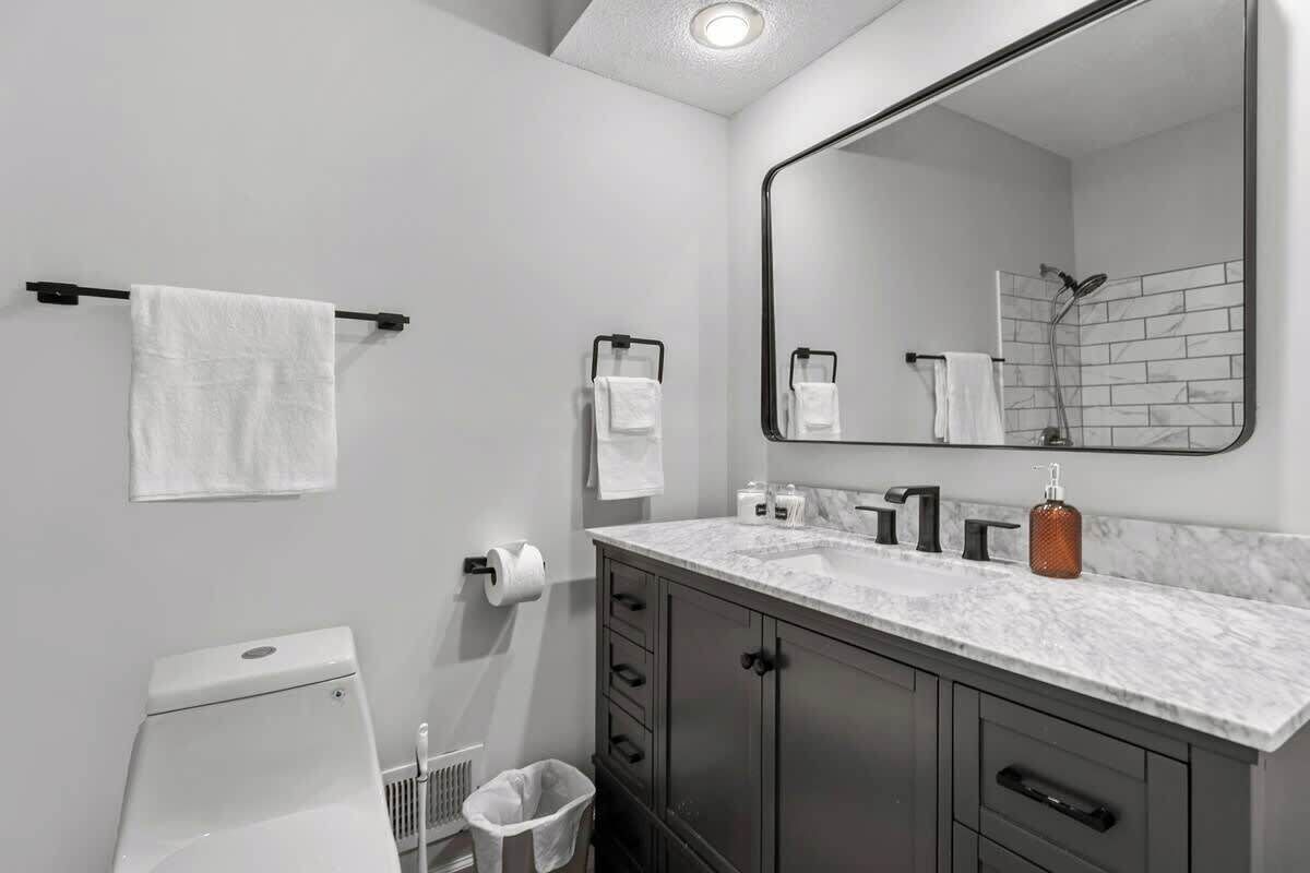Ein modernes Badezimmer mit Toilette, Waschbecken mit Marmorplatte, großem Spiegel und Handtuchhalter.