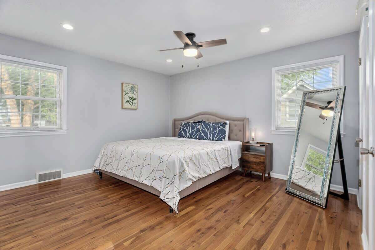 Une chambre à coucher avec un lit, une table de chevet, un miroir et un ventilateur de plafond.