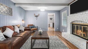 A living room with a brown leather sofa, a wooden coffee table, a fireplace, and a mounted deer head. - Family Fave w/2 Living Spaces_4BR_Great Location (Overland Park)