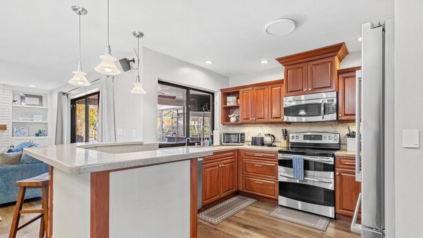 A modern kitchen with a central island, stainless steel appliances, wooden cabinets, and pendant lighting. - Family Home with Heated Pool_6 Mins from the Beach (Largo)