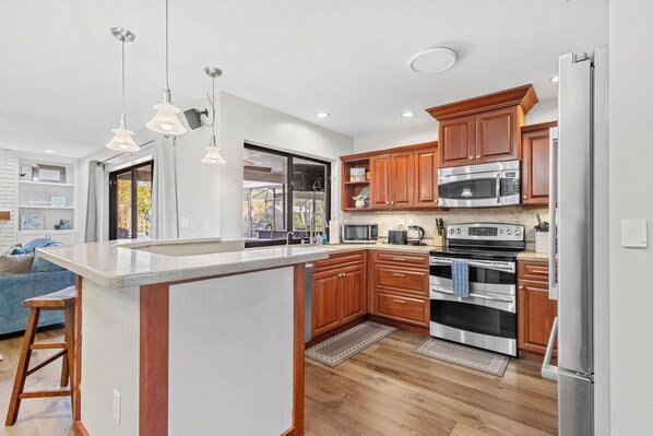 A modern kitchen with a central island, stainless steel appliances, wooden cabinets, and pendant lighting.