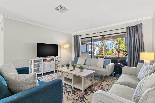A living room with a TV, sofa, and armchairs, a coffee table, and a view of the outdoors. - Family Home with Heated Pool_6 Mins from the Beach (Largo)