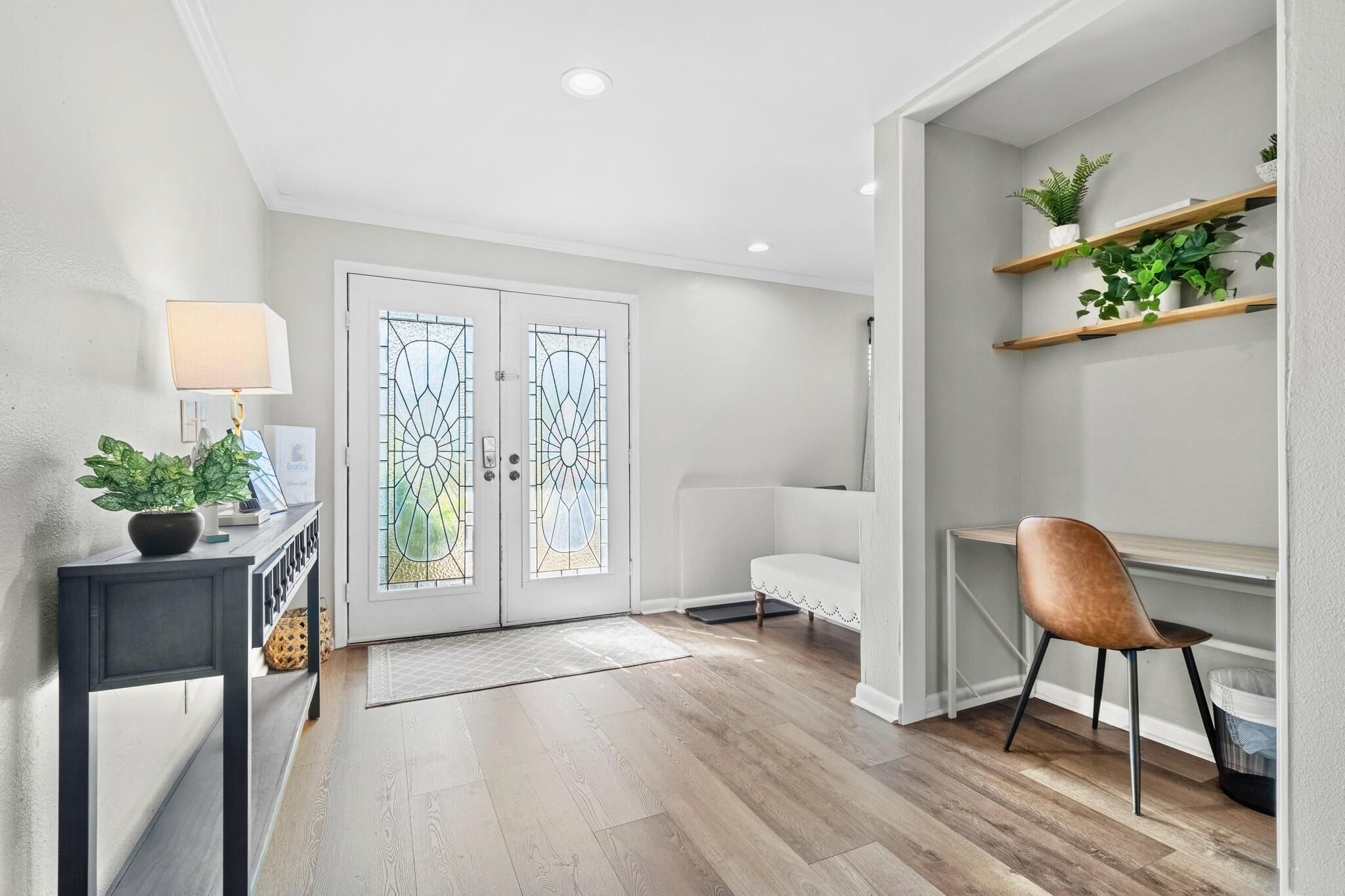 A modern hallway with a wooden floor, a white sofa, a brown chair, a desk with shelves, and a potted plant.