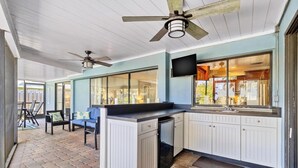 A covered outdoor kitchen area with a built-in refrigerator, a dining table with chairs, and a ceiling fan. - Family Home with Heated Pool_6 Mins from the Beach (Largo)