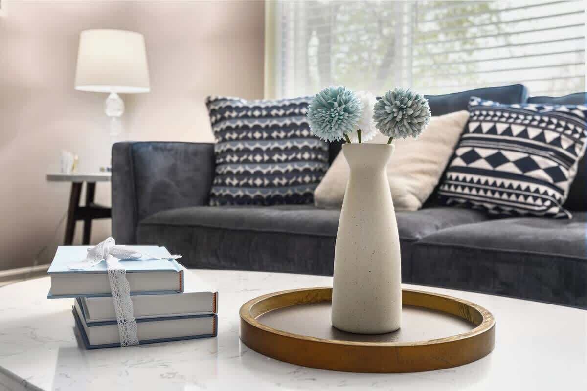 Ein Wohnzimmer mit einem weißen Couchtisch, einer Vase mit Blumen und einer Couch mit gemusterten Kissen.