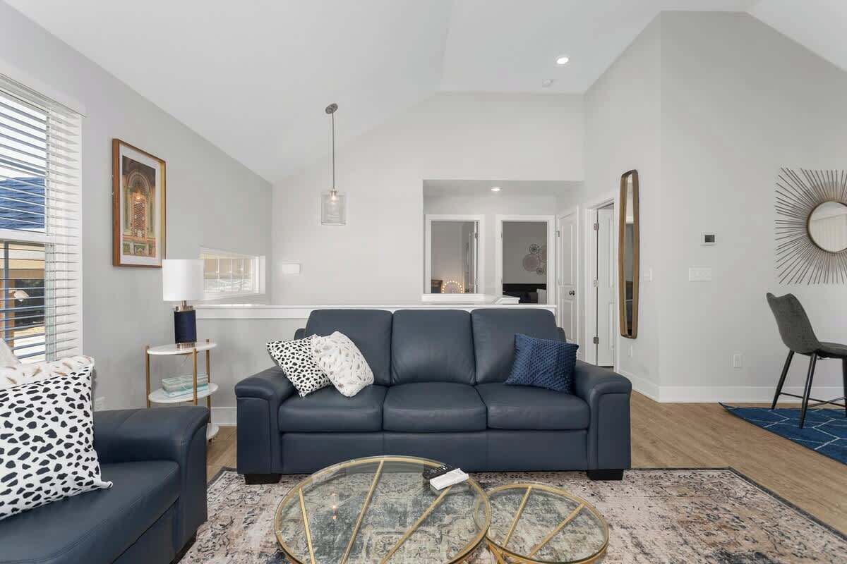 A modern living room with a dark grey sofa, a glass coffee table, and a patterned rug.