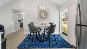 Una cocina moderna con un refrigerador de acero inoxidable, una mesa redonda con cuatro sillas y un tapete azul estampado.