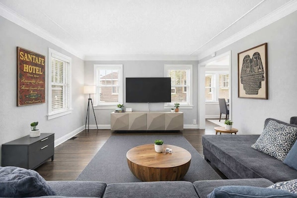 A modern living room with a flat-screen TV, grey sofas, a wooden coffee table, and a minimalist cabinet.