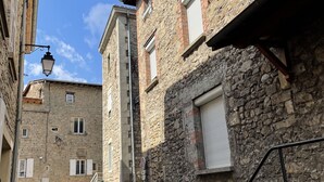 A narrow cobblestone street flanked by historic stone buildings with shuttered windows and a metal staircase. - Gîte des Serves apparently 40m2 Chavanay 5 people (Chavanay)