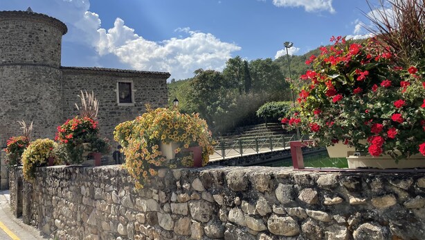 A stone building with a round tower, surrounded by stone walls and potted plants with red and yellow flowers. - Gîte des Serves apparently 40m2 Chavanay 5 people (Chavanay)