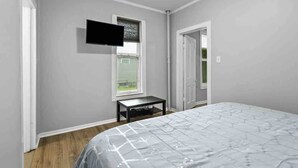 Ein Schlafzimmer mit einem Bett, einem an der Wand befestigten Fernseher, einem Fenster und einer Tür.