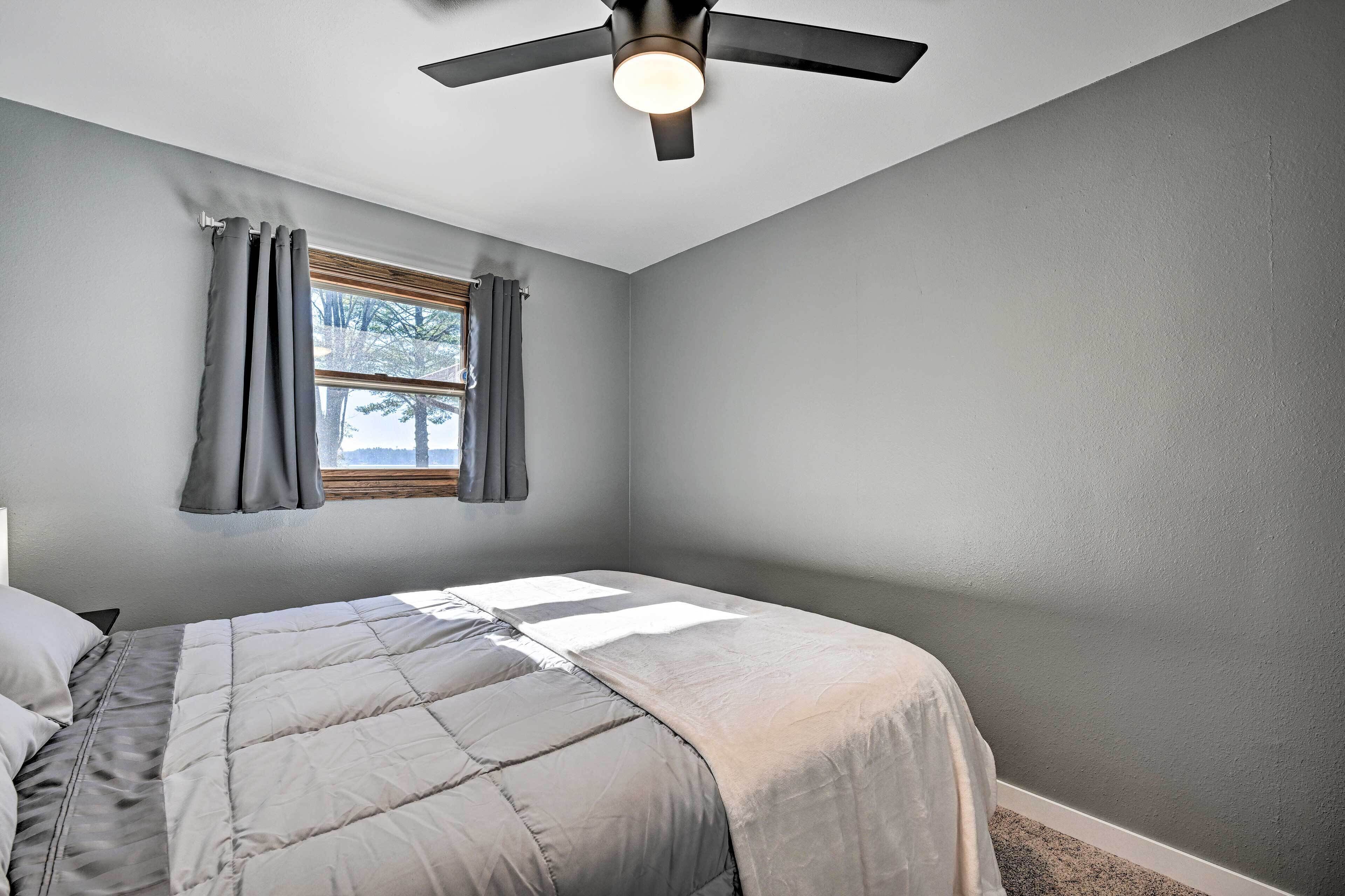 Un dormitorio con cama, ventilador de techo y ventana con cortinas.