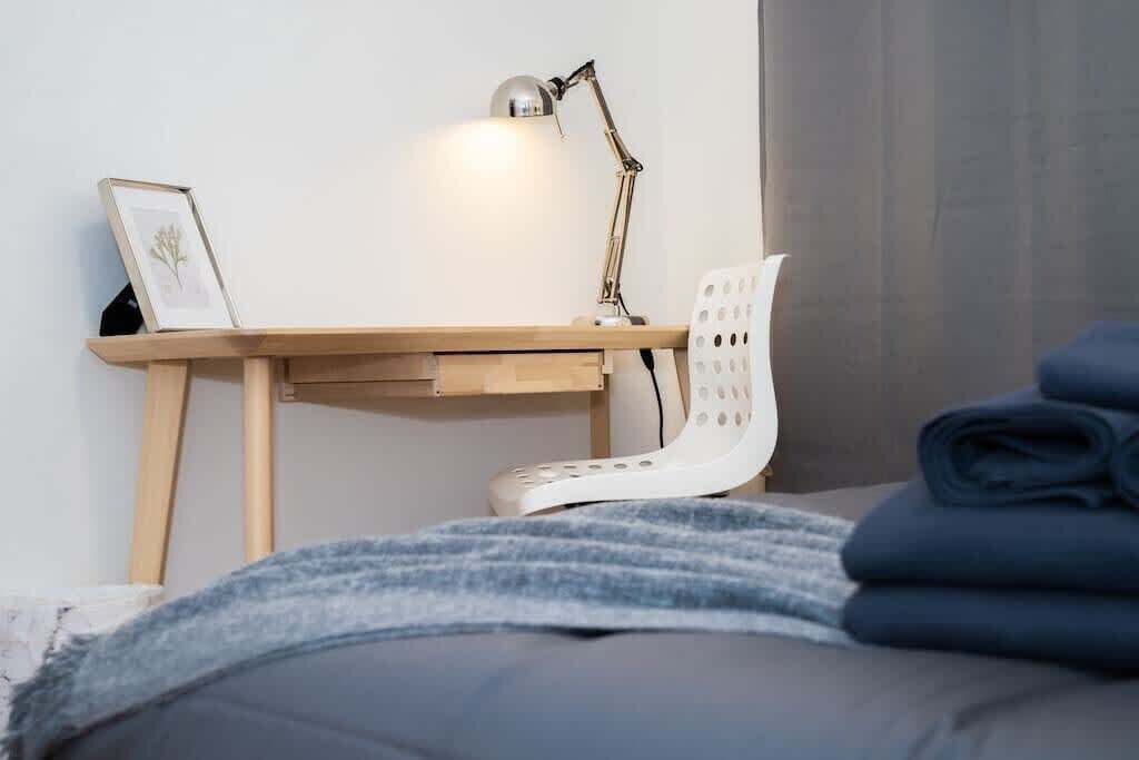 Une chambre à coucher bien rangée, avec un bureau en bois, une chaise blanche, un tableau encadré et une couverture pliée.