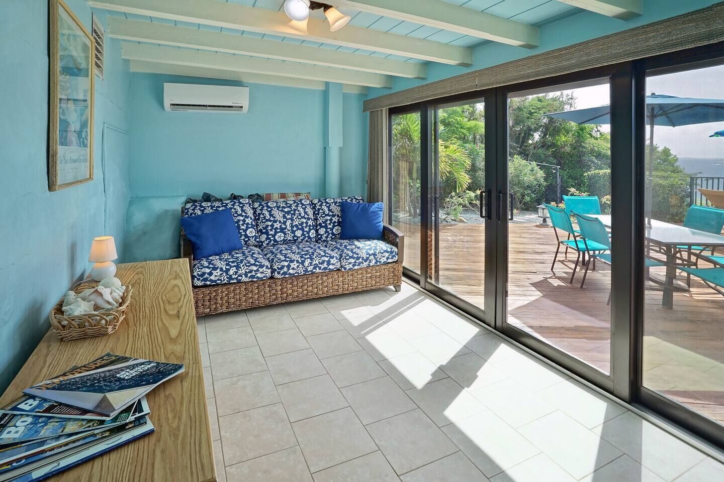 A room with a blue sofa, a wooden table with magazines, and a view of an outdoor patio with chairs and a table.