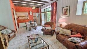 A living room with a brown leather sofa, a glass coffee table, and a dining area with a table and chairs. - Poppies - SAINT GILDAS (ST GILDAS)