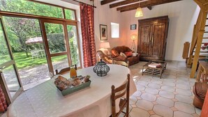 A cozy room with a dining table, chairs, a lamp, and a view of a garden through large windows. - Poppies - SAINT GILDAS (ST GILDAS)