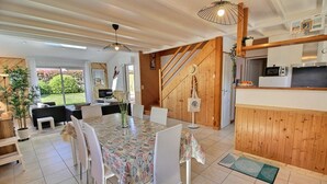 A modern kitchen with wooden accents, a dining area with a patterned tablecloth, and a view of a garden through large windows. - Ty Kaol - PERROS GUIREC (PERROS GUIREC)
