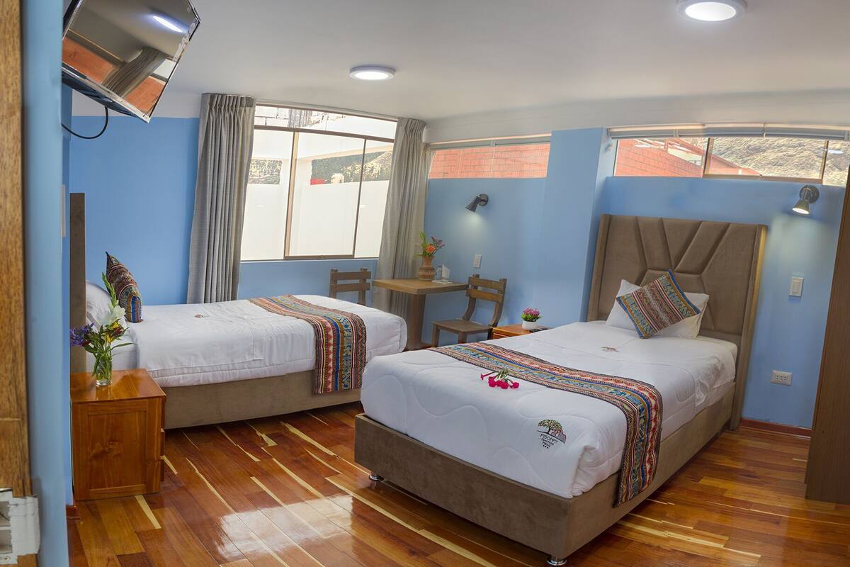 Una habitación de hotel con dos camas, una mesita pequeña, una silla, un escritorio y una ventana con cortinas.