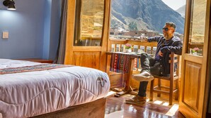 A room with a large bed, a wooden chair, and a balcony with a mountain view. - Pisonay Hotel (Pisac)