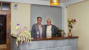 Two people standing at a reception desk with a decorative plant and a vase of flowers. - Pisonay Hotel (Pisac)