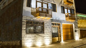 A two-story building with a stone facade, multiple balconies with wooden railings, and a garage entrance. - Pisonay Hotel (Pisac)