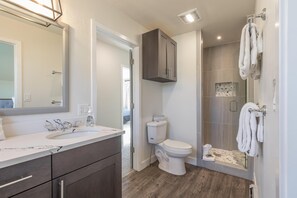Une salle de bain moderne avec un lavabo en marbre, des meubles sombres, des toilettes et une douche à l’italienne avec des parois en verre.