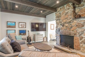 Ein Wohnzimmer mit Kamin aus Stein, einem Flachbildfernseher, einem Sofa und einer Gitarre.
