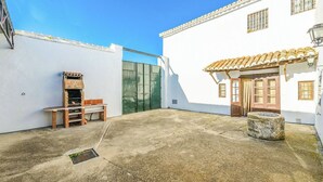 A courtyard with a brick barbecue, a green gate, and a white building with a tiled roof. - Huerta Nueva Cuevas del Becerro by Ruralidays (Málaga)
