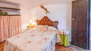 A bedroom with a bed, a nightstand with a lamp, a wooden door, and a curtain. - Huerta Nueva Cuevas del Becerro by Ruralidays (Málaga)