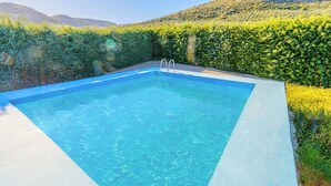 A rectangular swimming pool with a ladder, surrounded by a hedge and a hillside. - Huerta Nueva Cuevas del Becerro by Ruralidays (Málaga)