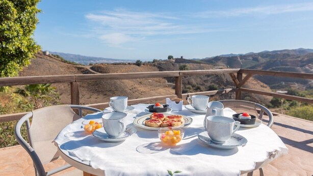 A table set for breakfast with cups, plates, and a pitcher, overlooking a scenic landscape.