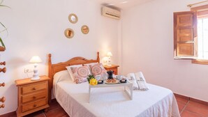 A neatly arranged bedroom with a bed, bedside tables, a nightstand, a bedside lamp, a small table with breakfast items, and decorative mirrors on the wall.
