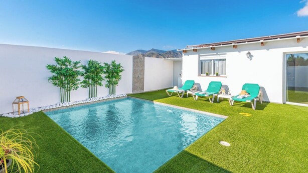 A swimming pool with artificial grass, a small garden with bamboo, and a building with a white exterior and a glass door. - Casa Flamenquita Nerja by Ruralidays (Málaga)