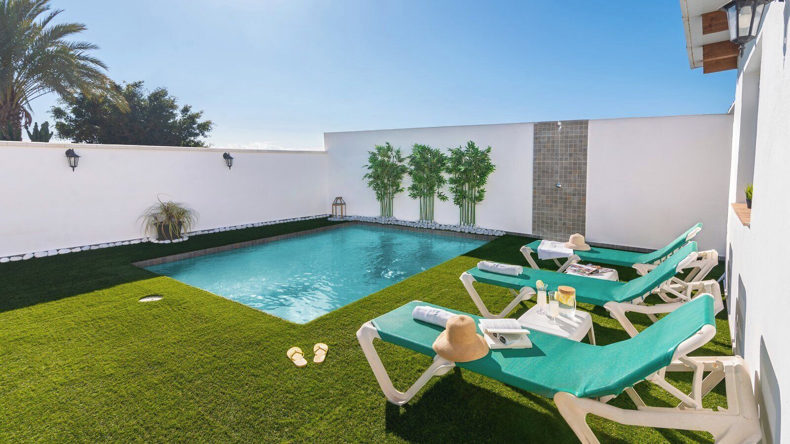 A swimming pool with a small grassy area and lounge chairs.