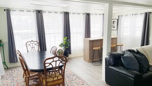 A modern living room with a dining area, featuring a black leather sofa, wooden dining table, and chairs. - The Club House - Suite 101 (Sault Ste. Marie)
