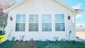 A white single-story house with four windows and two exterior wall-mounted lanterns. - The Club House - Suite 101 (Sault Ste. Marie)
