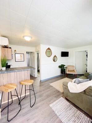 Een moderne woonkamer met houten vloer, een bank, een salontafel en een aan de muur bevestigde televisie.