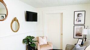 Ein Wohnzimmer mit einem beigen Teppich, zwei Sofas, einem Sessel, einem an der Wand montierten Fernseher und einer Tür.