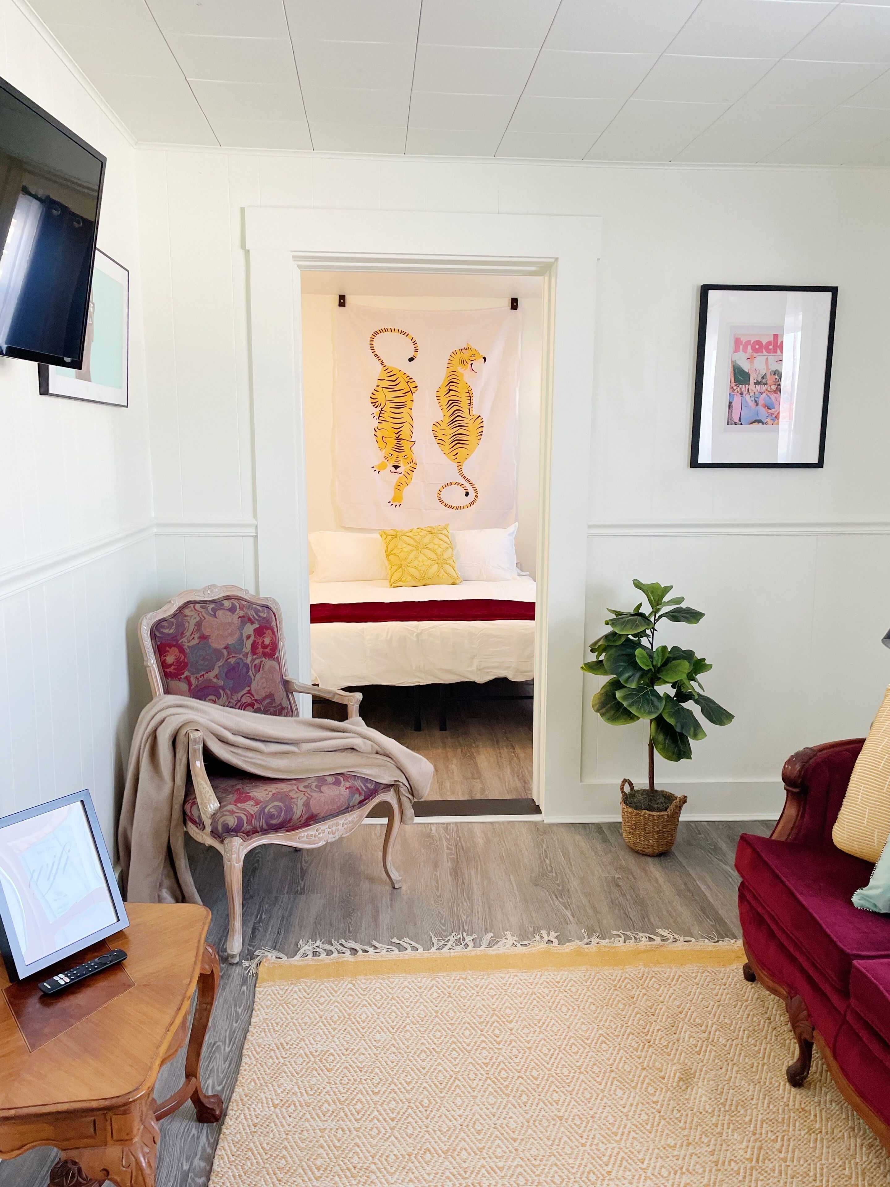 Een kamer met een bed, een stoel, een tafeltje, een televisie en een plant.