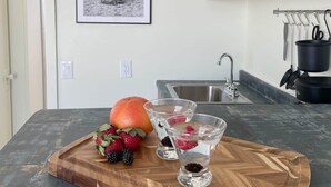 Une cuisine avec un plan de travail en bois, un four à micro-ondes et un évier. Un cadre contenant une photographie en noir et blanc est accroché au mur, et un panier de fruits contenant des baies et une orange est posé sur le plan de travail.